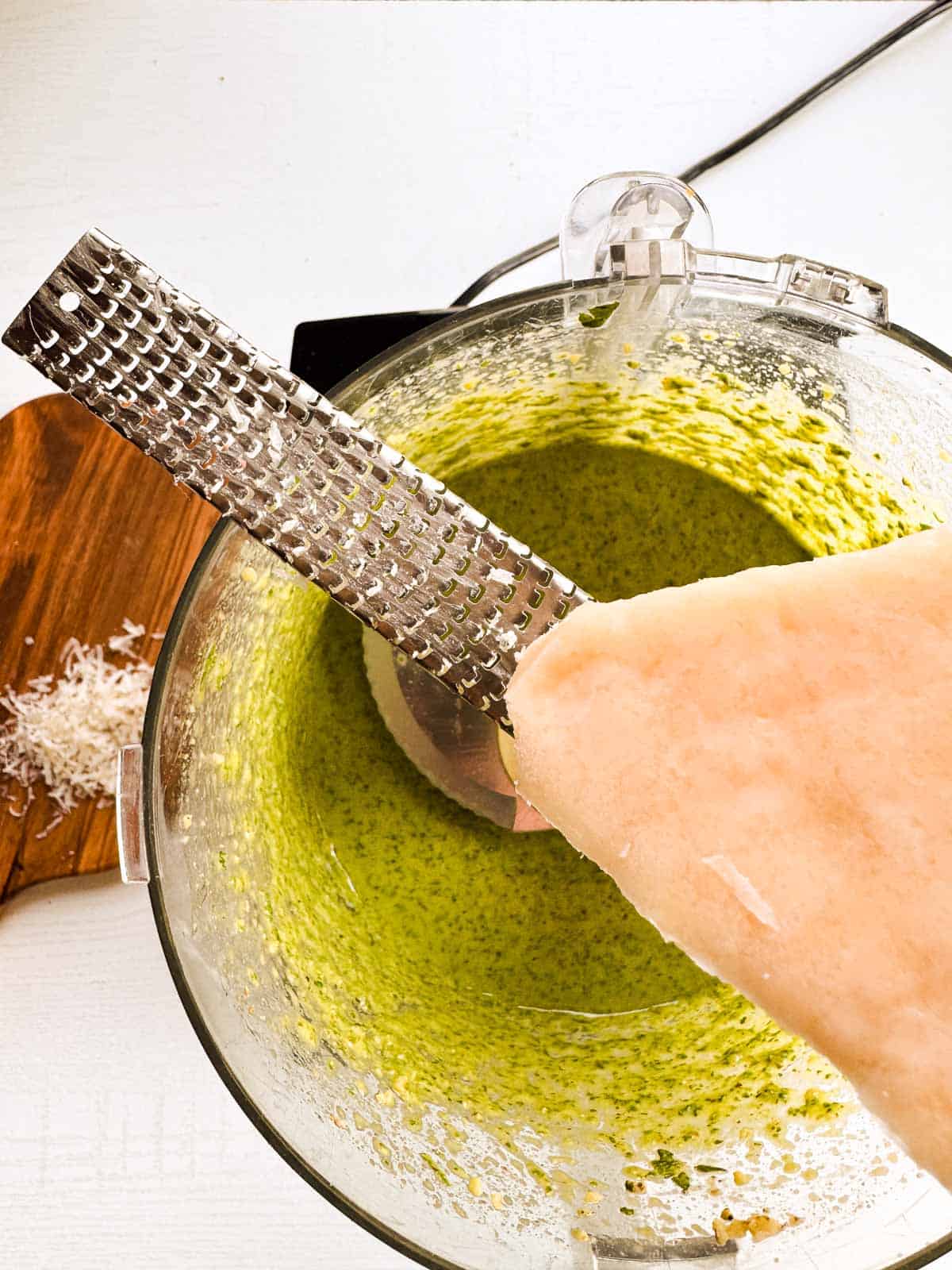 wedge of parmesan cheese with a microplane over a food processor.