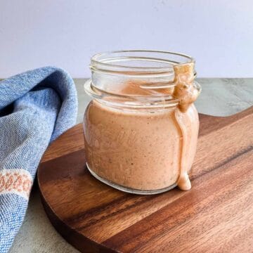 wide mouth mason jar with low fodmap thousand island dressing with a bit dripping down the side while sitting on a wooden board and sitting alongside a napkin.