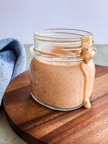 wide mouth mason jar with low fodmap thousand island dressing with a bit dripping down the side while sitting on a wooden board and sitting alongside a napkin.