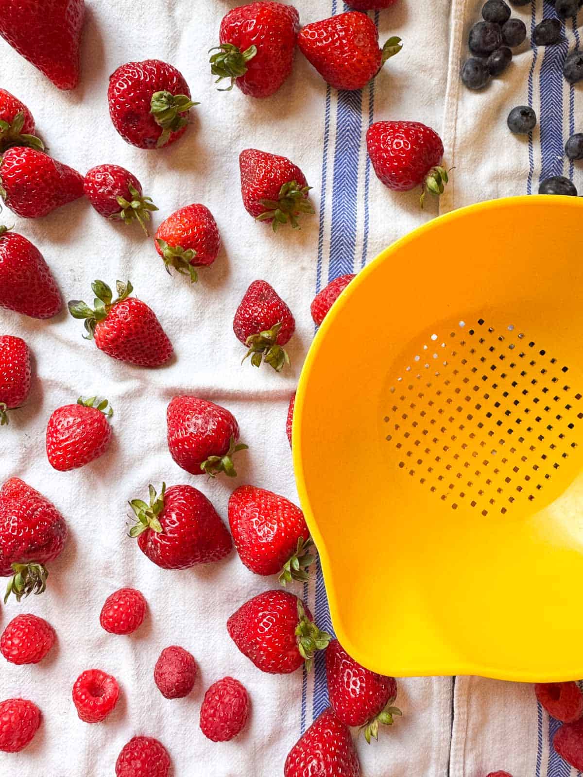 yellow tupperware strainer with assorted berries drying on a flour sack towel.