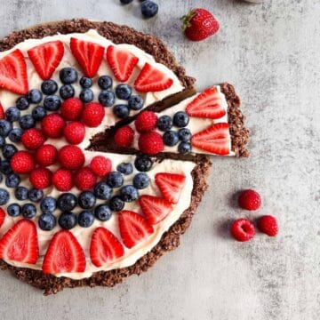 gluten free fruit pizza with a slice cut out alongside fresh berries.
