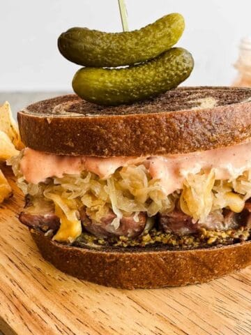 bratwurst sandwich on a wooden cutting board with kettle chips and pickles.