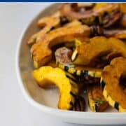 Close-up of roasted delicata squash slices with pecans in a white serving dish.