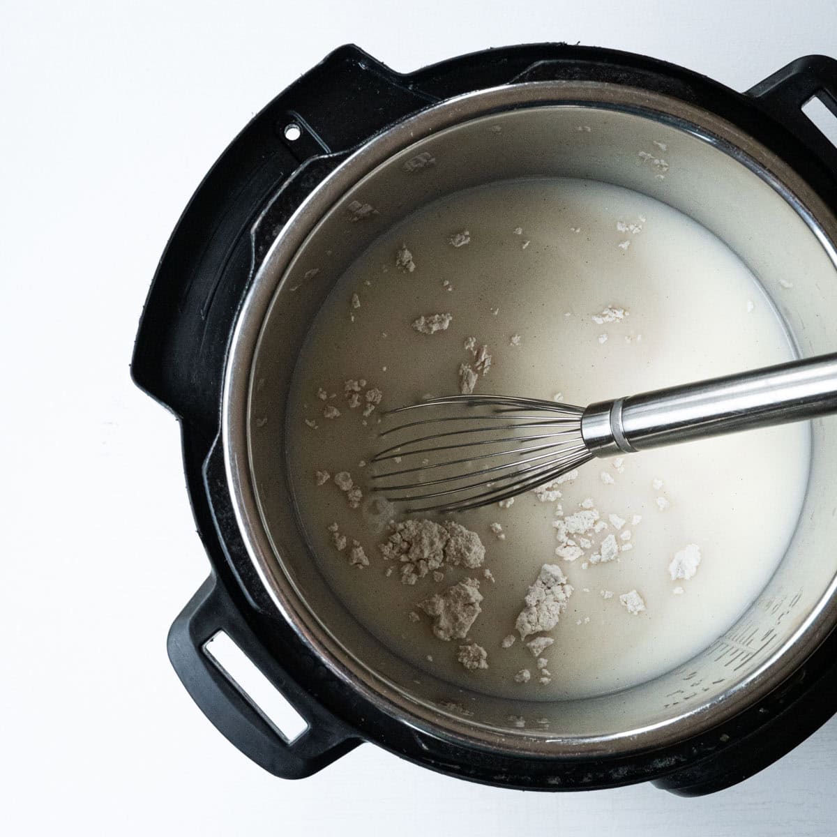 inside an instant pot with chicken broth, milk and flour with a whisk.
