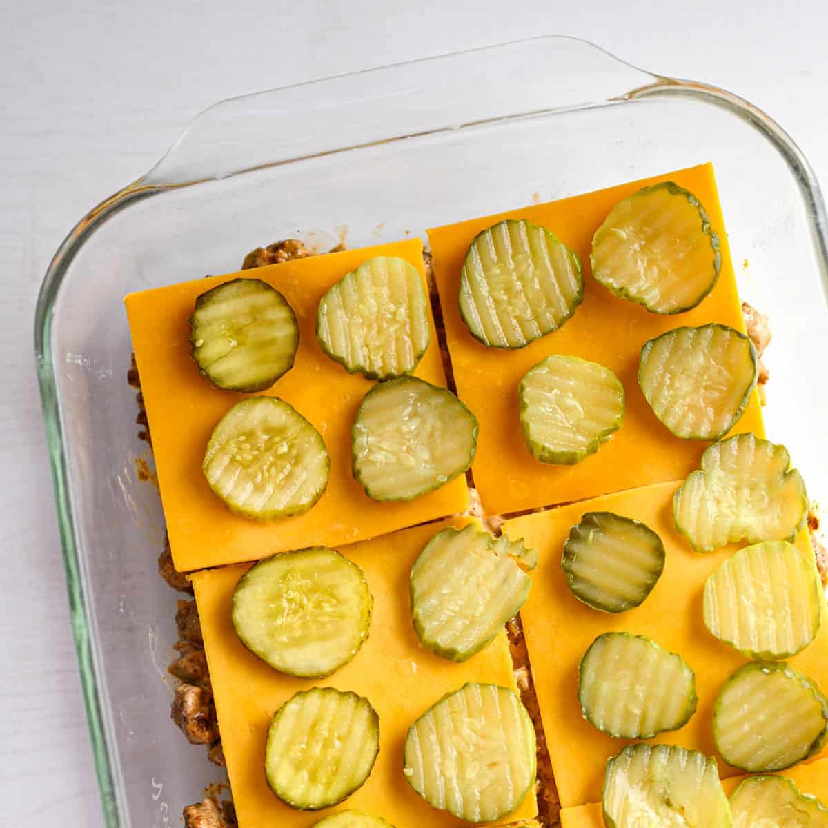baking dish with meat mixture layer on top with cheese slices and then pickles.