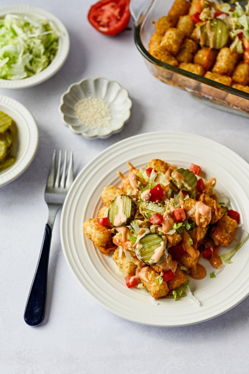 plate with a serving of big mac tater tot casserole along with additional toppings and an entire baking dish full of casserole.