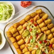 overhead shot of big mac tater tot casserole topped with shredded lettuce, diced tomatoes, pickles, thousand island dressing and sesame seeds.