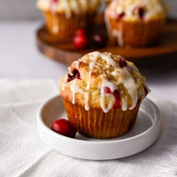 one cranberry orange muffin on a white dish with a few muffins in the background on a wooden board.