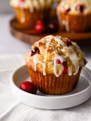 one cranberry orange muffin on a white dish with a few muffins in the background on a wooden board.