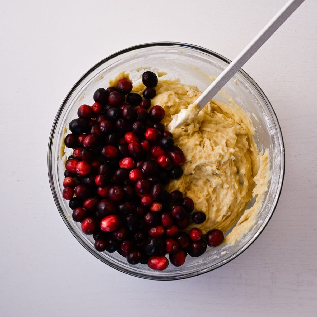 mixed muffin batter with whole cranberries in a glass bowl.