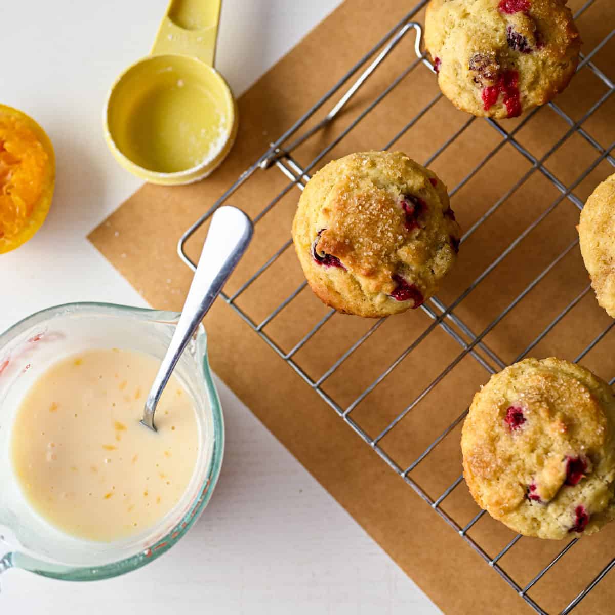 cooled muffins on a cooling rack alongside a glaze, measuring cup and a squeezed orange.