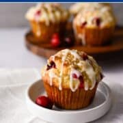 a gluten free cranberry orange muffin on a small white dish with a few muffins in the background on a wooden board.