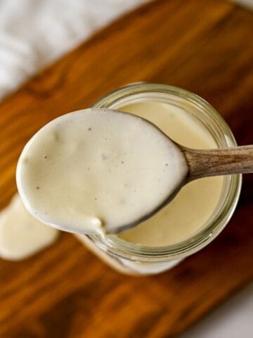 wooden spoon full of Caesar dressing above a mason jar on a wooden board.