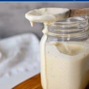 mason jar full of caesar dressing topped with a wooden spoon on a wooden board.
