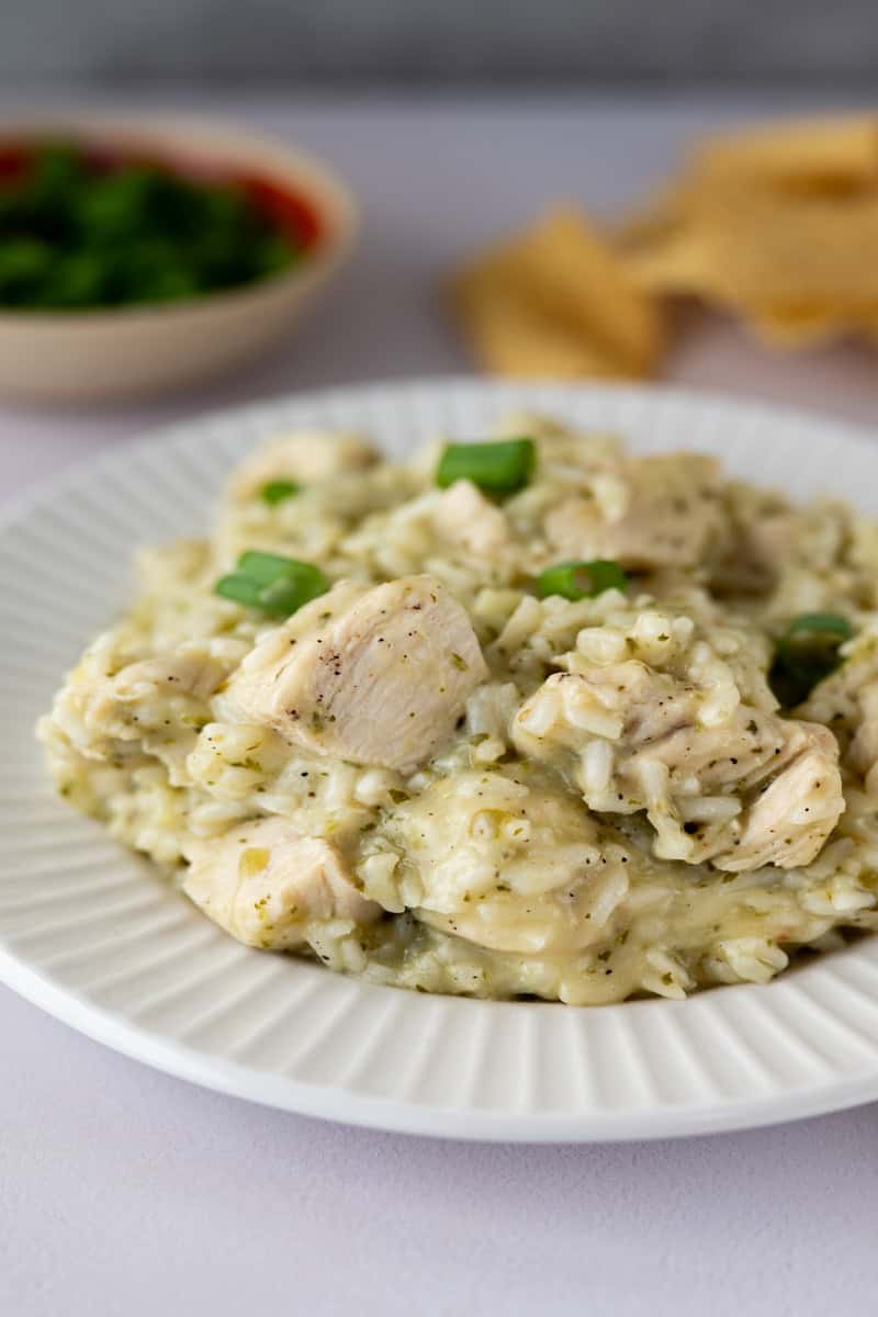 plate of salsa verde chicken and rice with a small dish of salsa and handful of tortilla chips in the background.