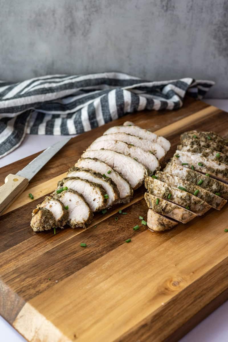 two sliced turkey tenderloins on a wooden cutting board along with a knife and napkin.