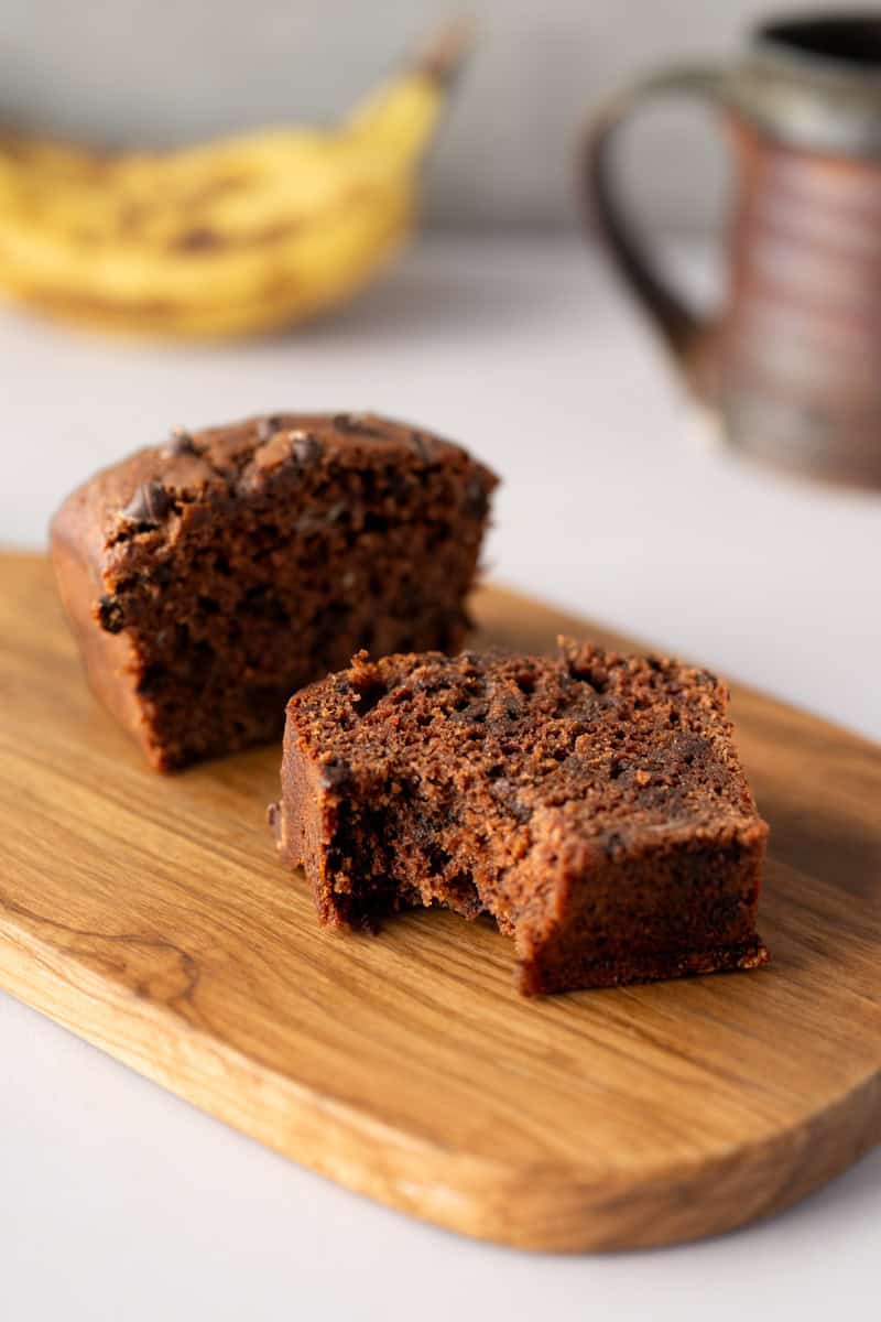 sliced chocolate banana bread with a bite missing on a wooden cutting board.