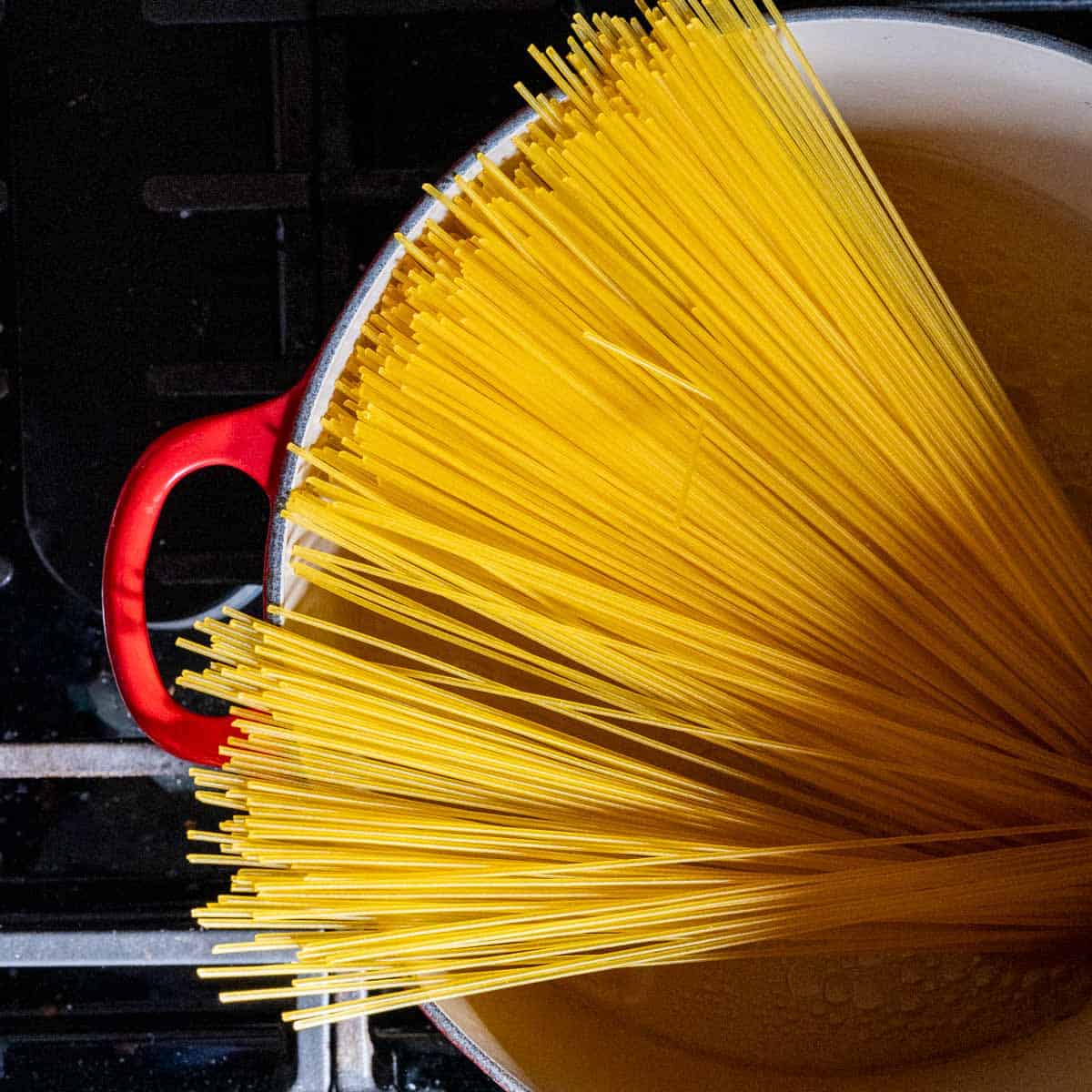 spaghetti noodles in a red dutch oven filled with chicken stock and garlic oil.