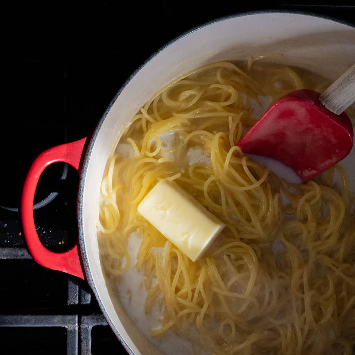 cooked pasta with milk and butter added to the red dutch oven.