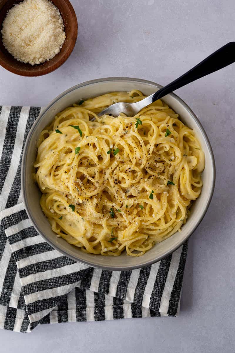 bowl full of cooked spaghetti noodles with a fork and a small dish of parmesan cheese.