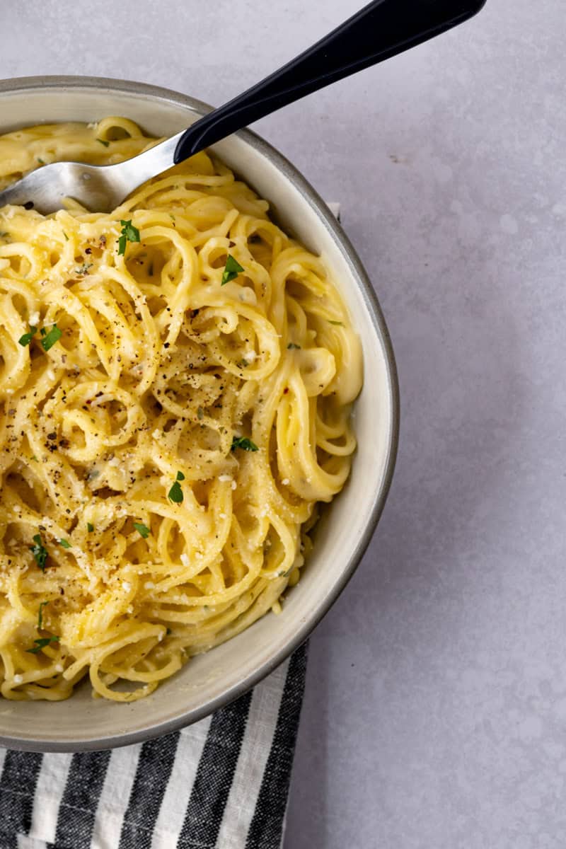 overhead view of creamy parmesan pasta topped with parmesan cheese, black pepper and fresh parsley.