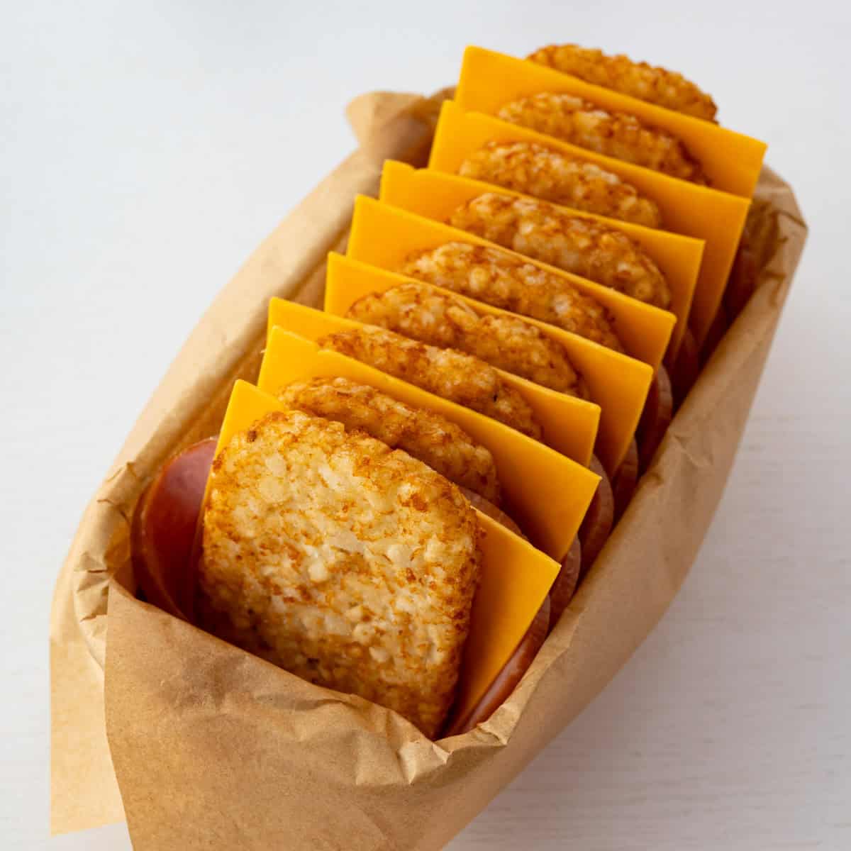 parchment lined loaf pan with layered hash brown patties, sliced ham, and cheddar cheese.
