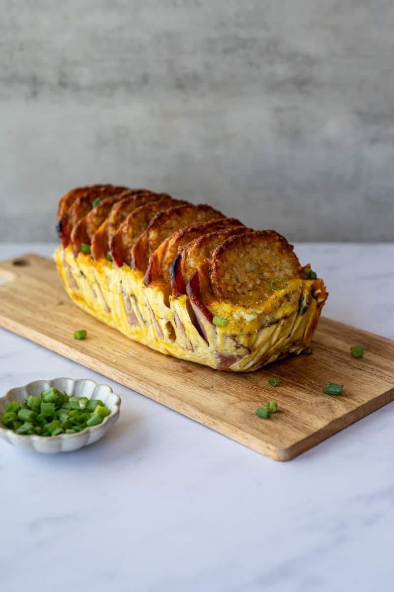 breakfast casserole removed from the parchement paper sitting on a wooden board alongside chopped green onions.
