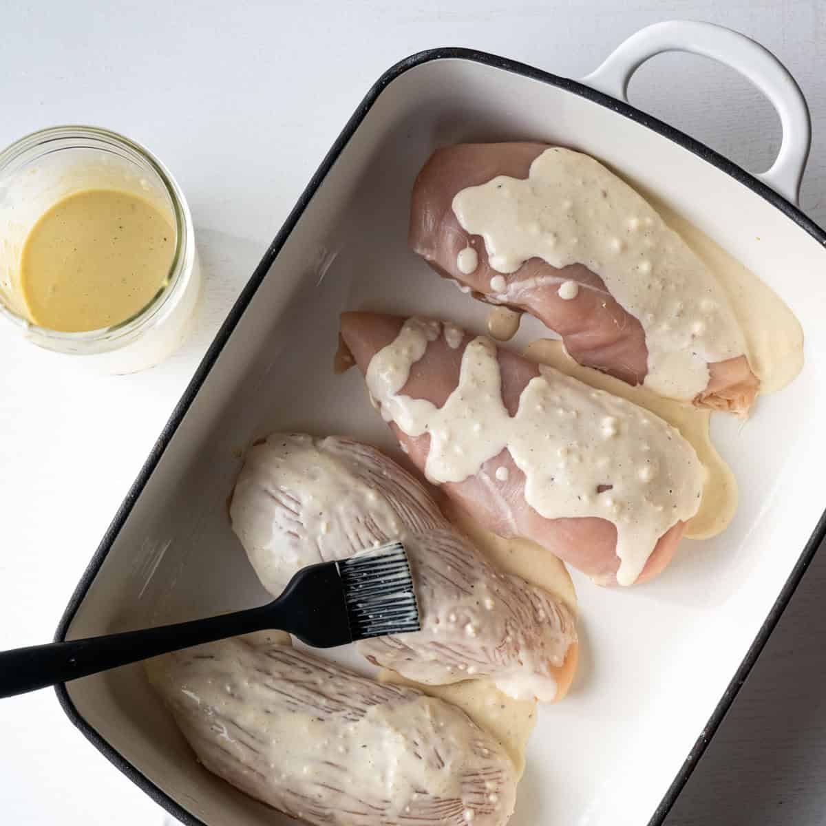 caesar dressing brushed on chicken breasts in a white baking dish.