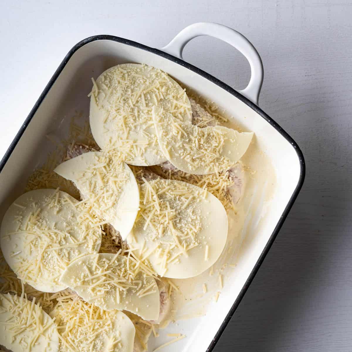 provlone and shredded parmesan cheese topping chicken breasts in a baking dish.