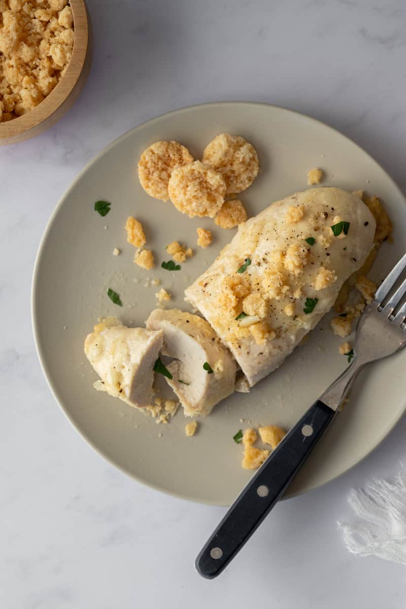 sliced chicken breasts on a plate with a fork and crushed parmesan cheese crisps.