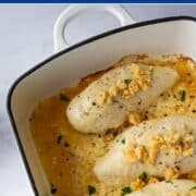 A close-up shot of baked Caesar chicken in a casserole dish, featuring a golden cheesy sauce and a sprinkling of Parmesan crisp crumbs.