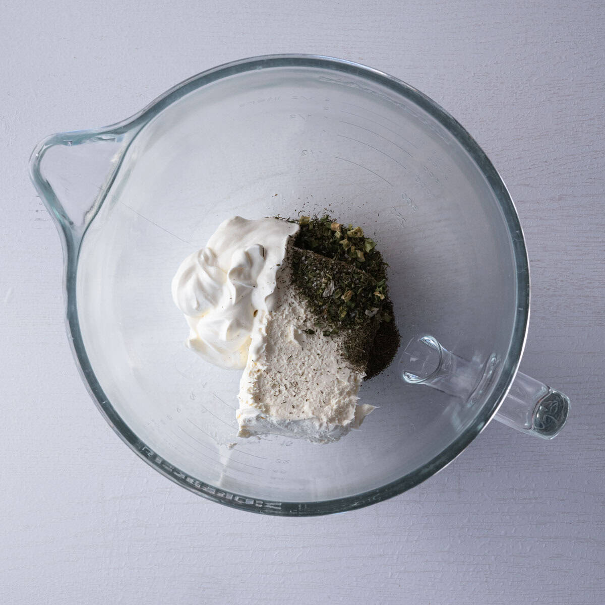 glass bowl of cream cheese, sour cream, ranch seasoning and dill.
