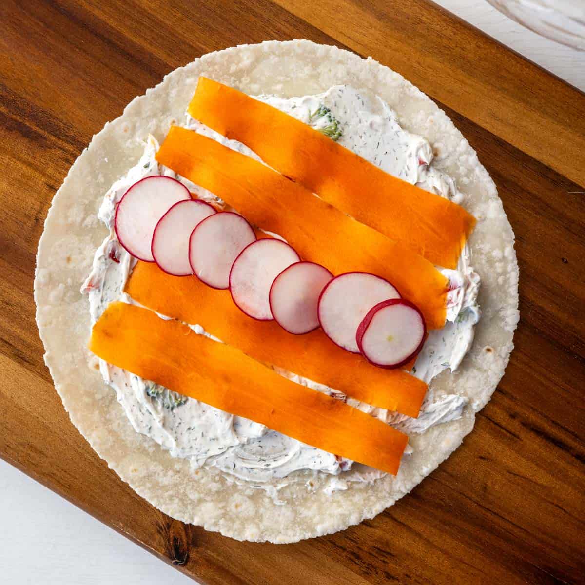 a gluten free tortilla, carrot ribbons and sliced radishes on a wooden cutting board.