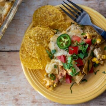 yellow plate with a serving of green chile chicken casserole with toppings and a handful of tortilla chips.