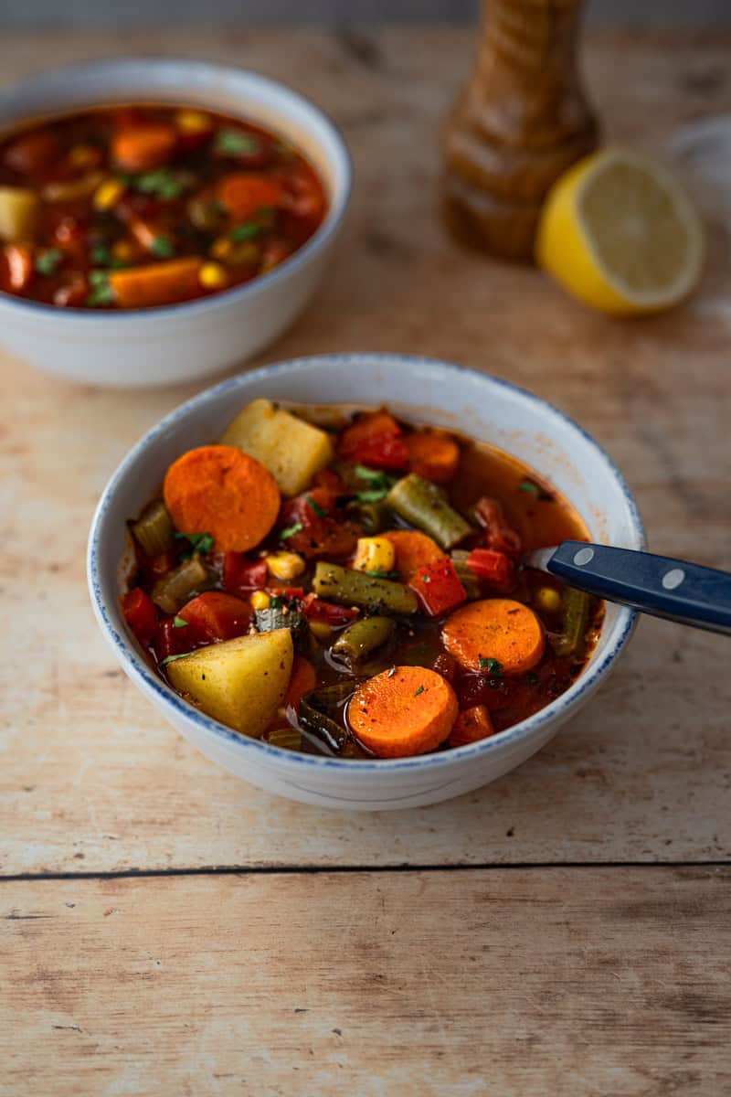 two bowls full of vegetable soup with a peppermill and squeezed lemon in the background.