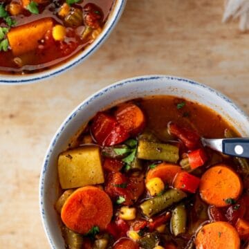 two bowls of vegetable soup with a spoon in one.