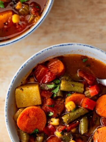 two bowls of vegetable soup with a spoon in one.