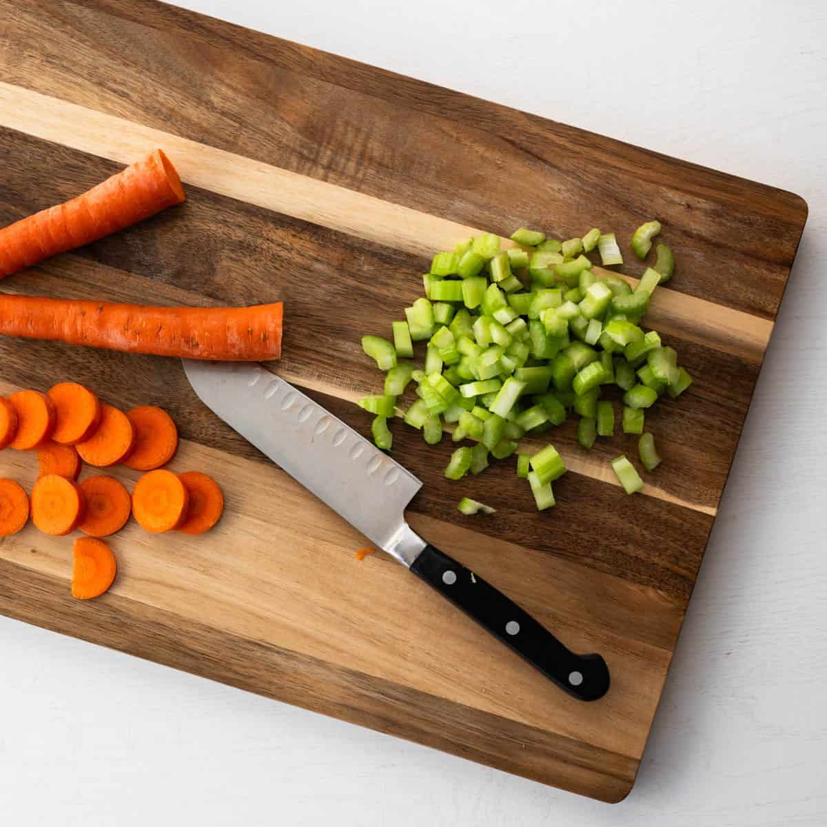 chopped carrots and celery on a wooden board with a knife.