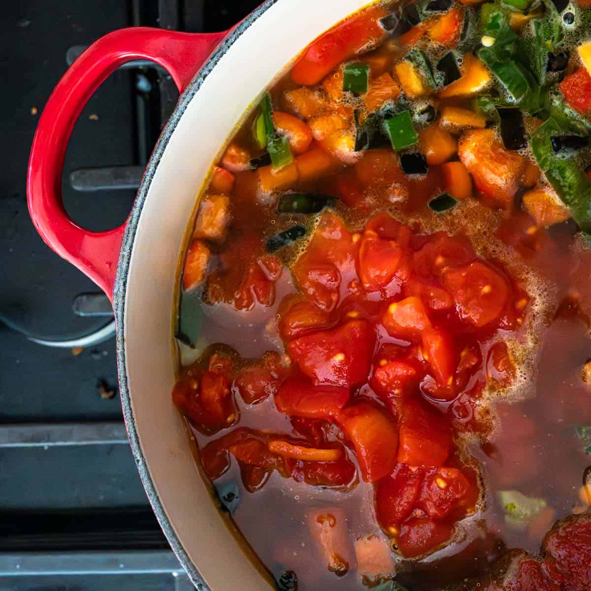 diced tomatoes added to the red dutch oven full of veg soup.