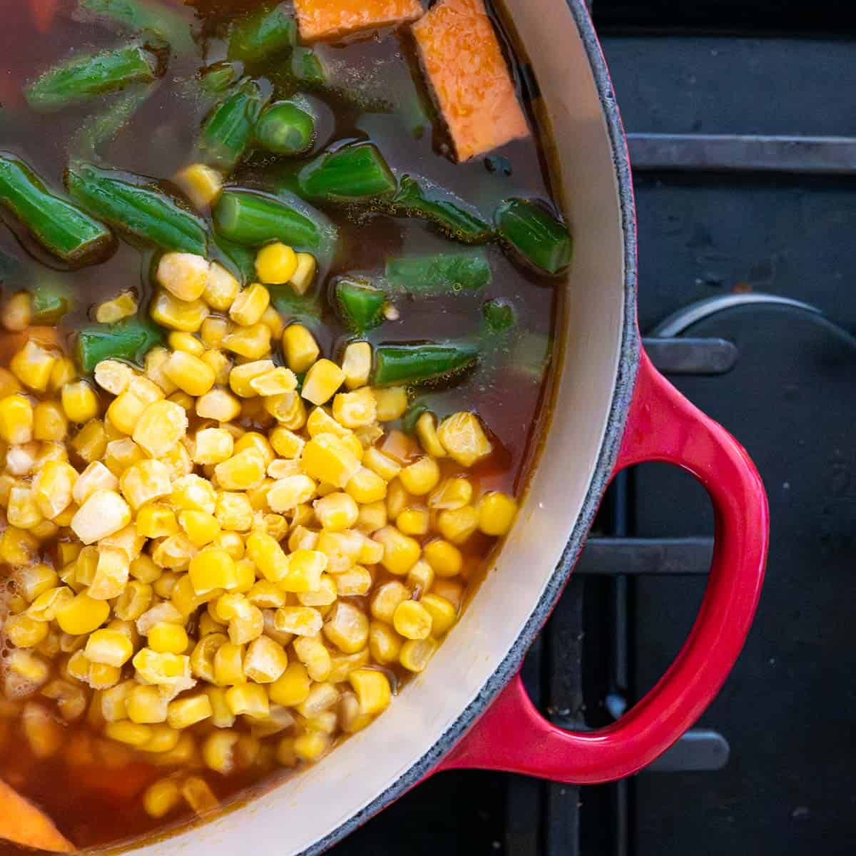 corn and green beans added to the vegetable soup in red dutch oven.