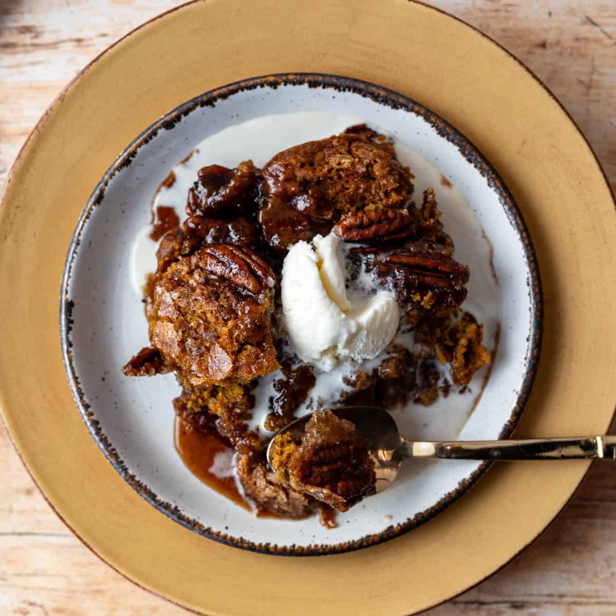 plate with a serving of pumpkin cake topped with ice cream with a spoon.