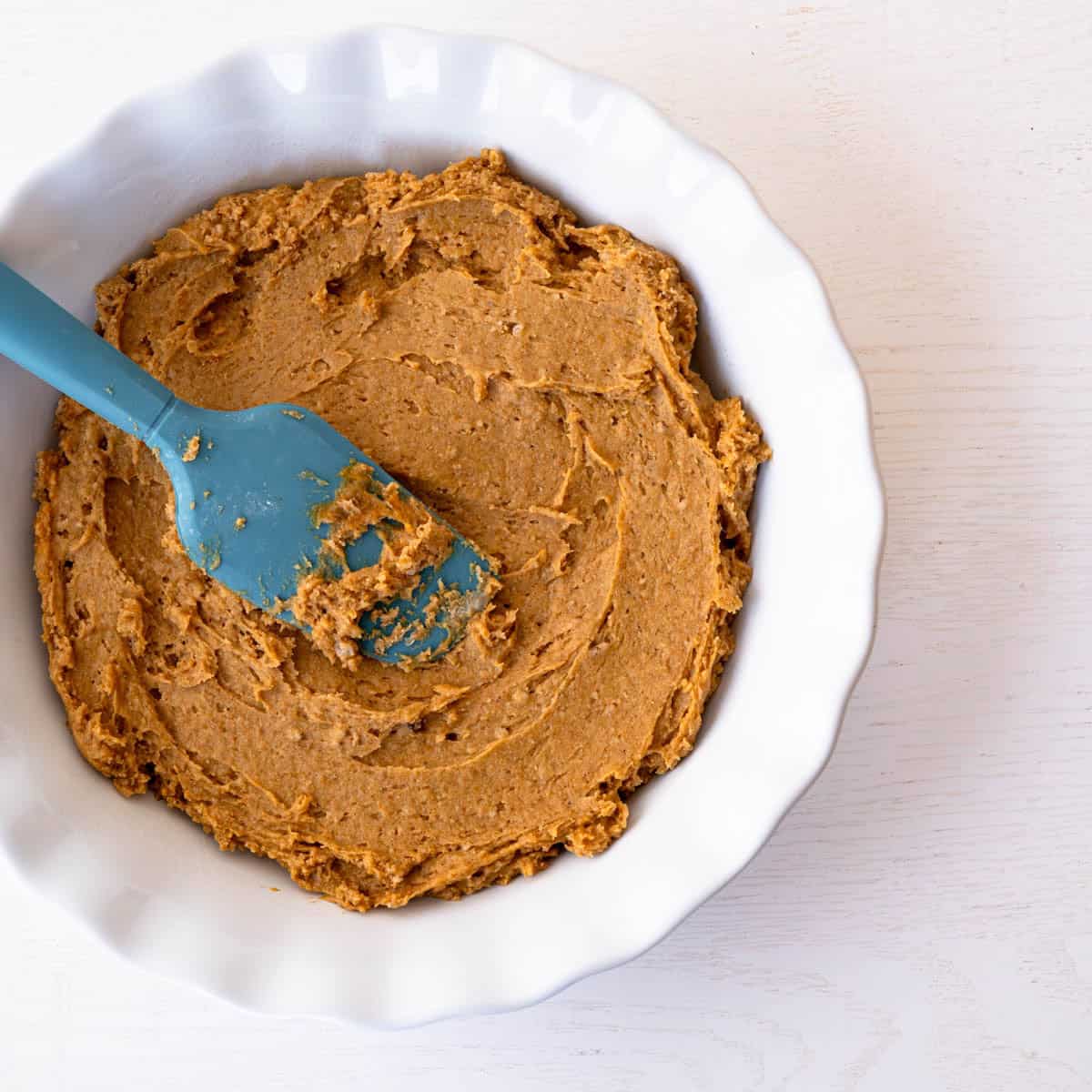 the cake batter spread evenly into a baking dish with a blue spatula.