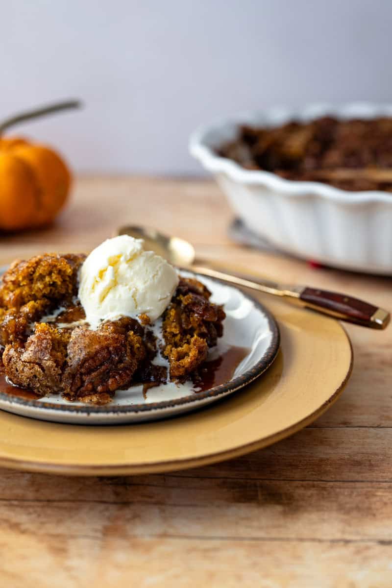 serving of pumpkin cake on a plate topped with ice cream with a pie plate in the background.