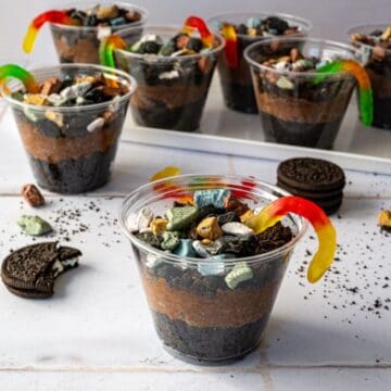 multiple dirt cake cups topped with candy rocks and gummy worms.