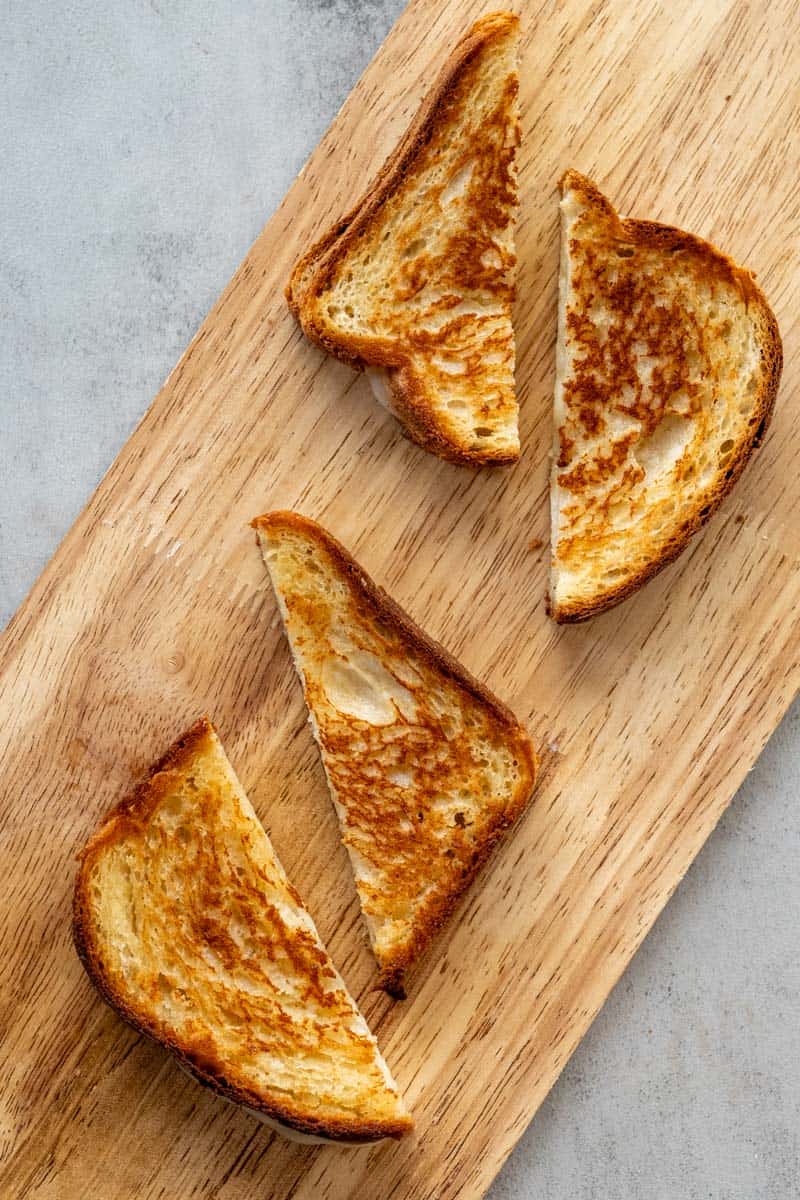 two grilled cheese sandwiches sliced in half on a wooden board.