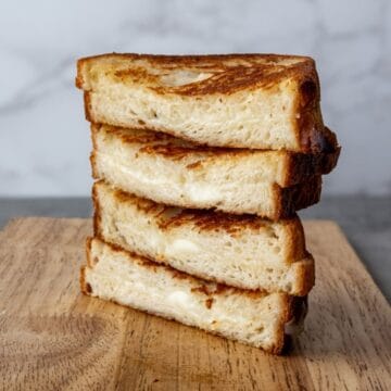 four grilled havarti cheese sandwiches stacked on a wooden board.