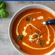 bowl of low FODMAP tomato soup swirled with a bit of heavy cream and topped with fresh basil and black pepper.
