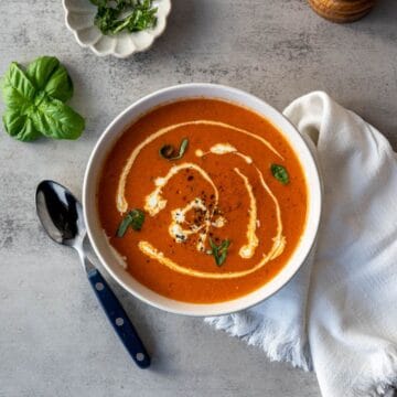 bowl of homemade tomato soup swirled with heavy cream and topped with fresh basil, black pepper.