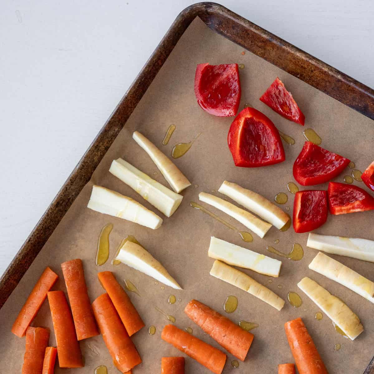 cut up red bell pepper, parsnips, carrots on a baking sheet.
