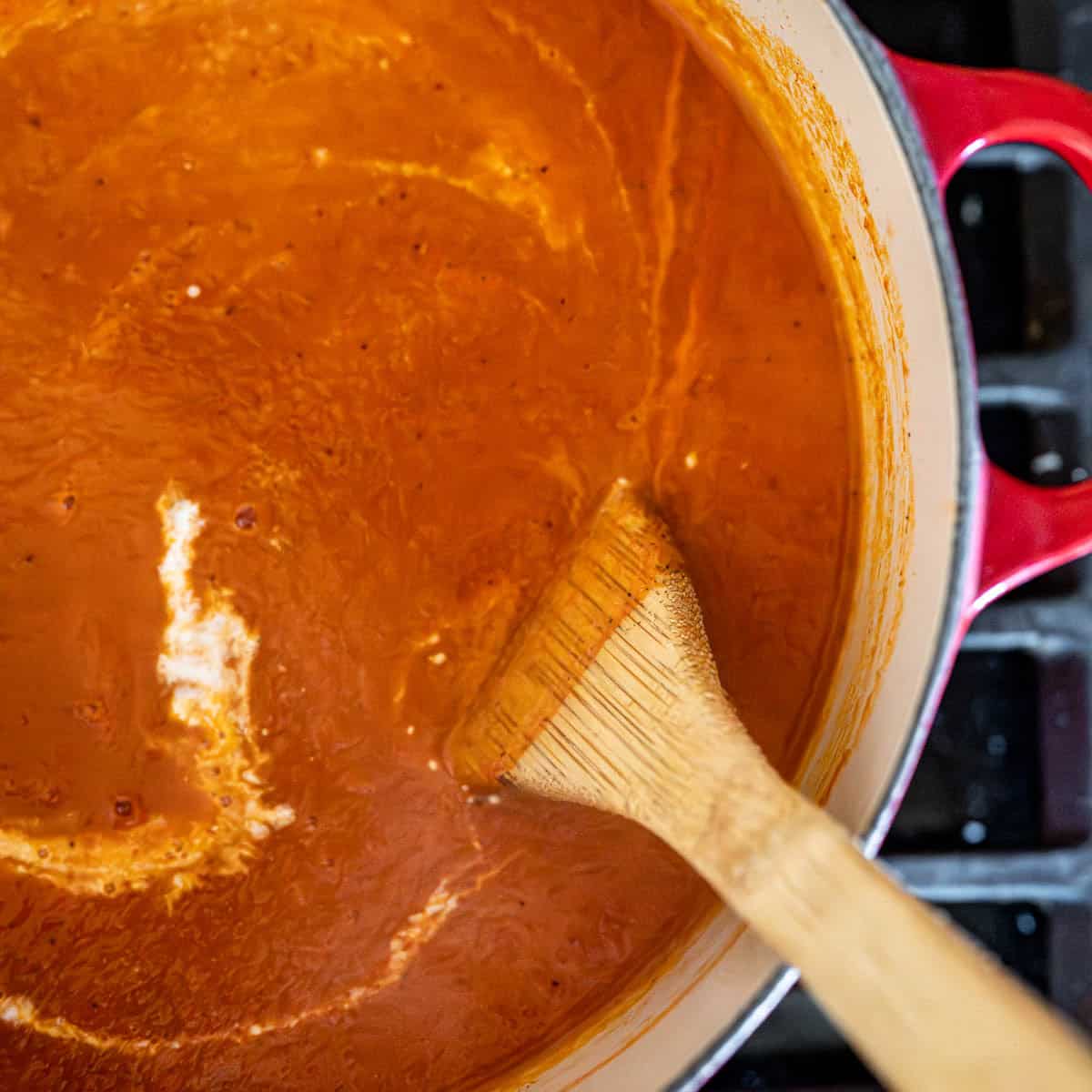 heavy cream poured into the tomato soup with a wooden spoon.